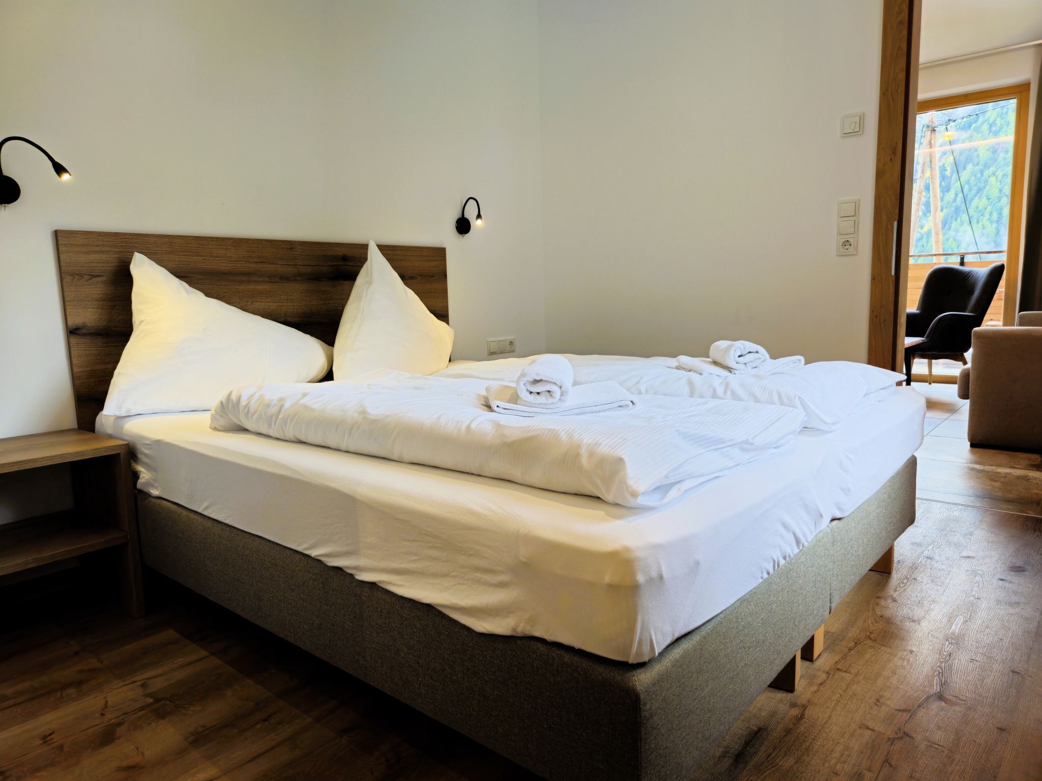 A neatly made bed with white linens and towels, a wooden headboard, and a nightstand.