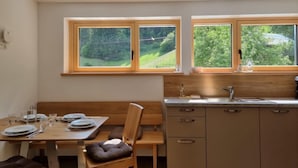 A modern kitchen with wooden cabinets, a sink, and two windows offering a view of greenery. - Home Fuchsbau by Interhome (See)