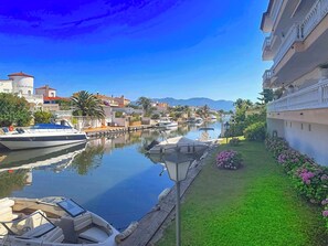 A marina with boats docked, a grassy area with flowers, and buildings with balconies.