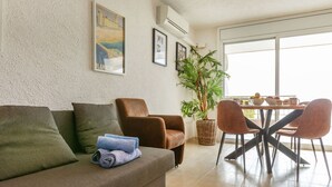 Ein Wohnzimmer mit einer Couch, Sesseln, einem Esstisch mit Stühlen, einer Zimmerpflanze und gerahmten Bildern an der Wand.