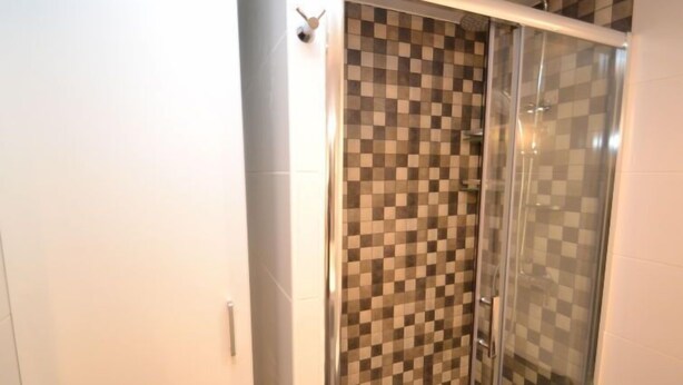 A bathroom with a glass shower enclosure, checkered tile walls, and a white door. - Salourhin by Interhome (Salou)