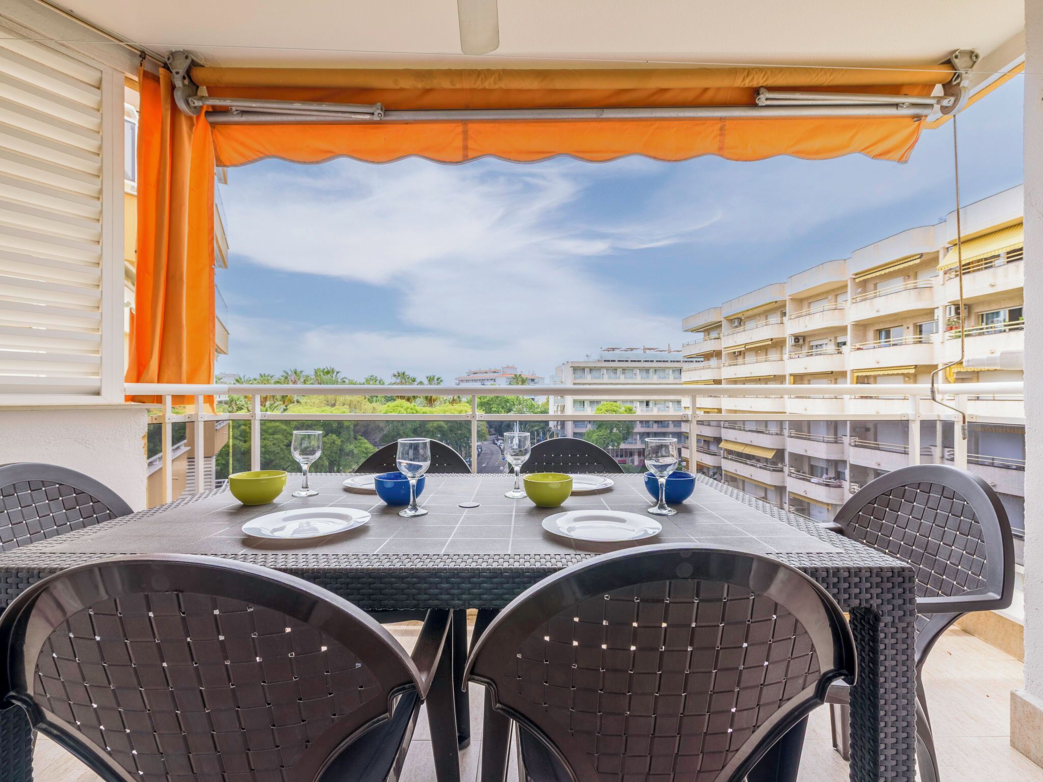 A balcony with a table set for four, chairs, and a view of buildings and greenery.