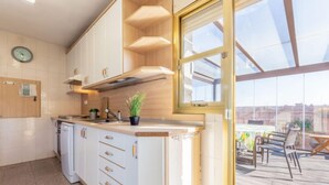 Une cuisine moderne avec des armoires blanches, un four encastré et une fenêtre donnant sur une terrasse.