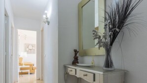 Un couloir avec une coiffeuse blanche, un miroir et un vase contenant des plantes séchées.