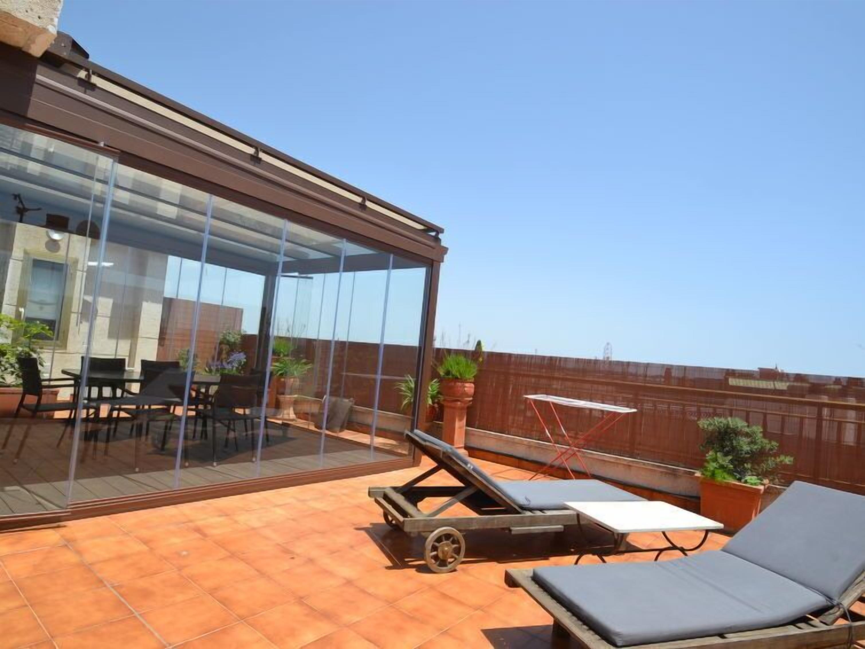 A rooftop terrace with a glass enclosure, outdoor seating, and lounge chairs.