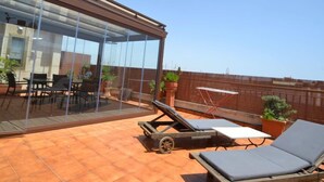 Une terrasse sur le toit, dotée d’une structure vitrée, d’un espace salon extérieur et de chaises longues.