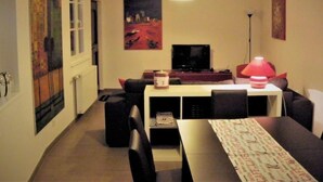 Ein gemütliches Wohnzimmer mit Fernseher, Tisch mit Lampe und Kunstwerken an den Wänden.