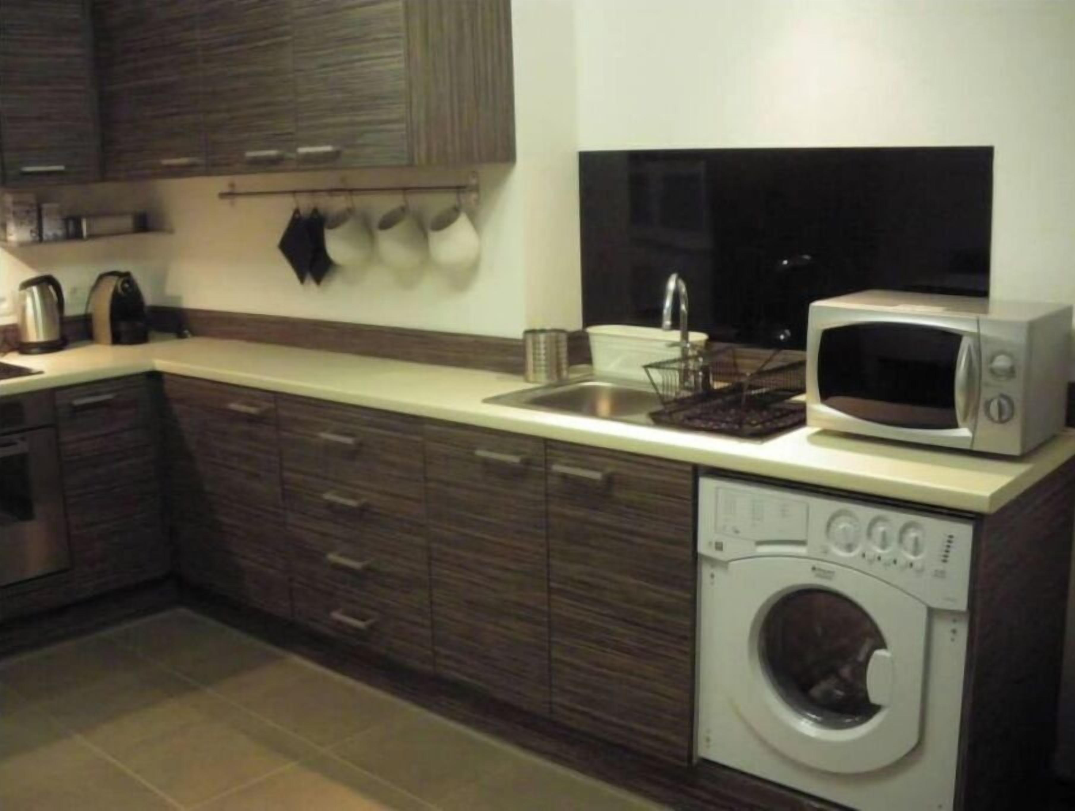A modern kitchen with wooden cabinets, a built-in washing machine, a microwave, and a sink.