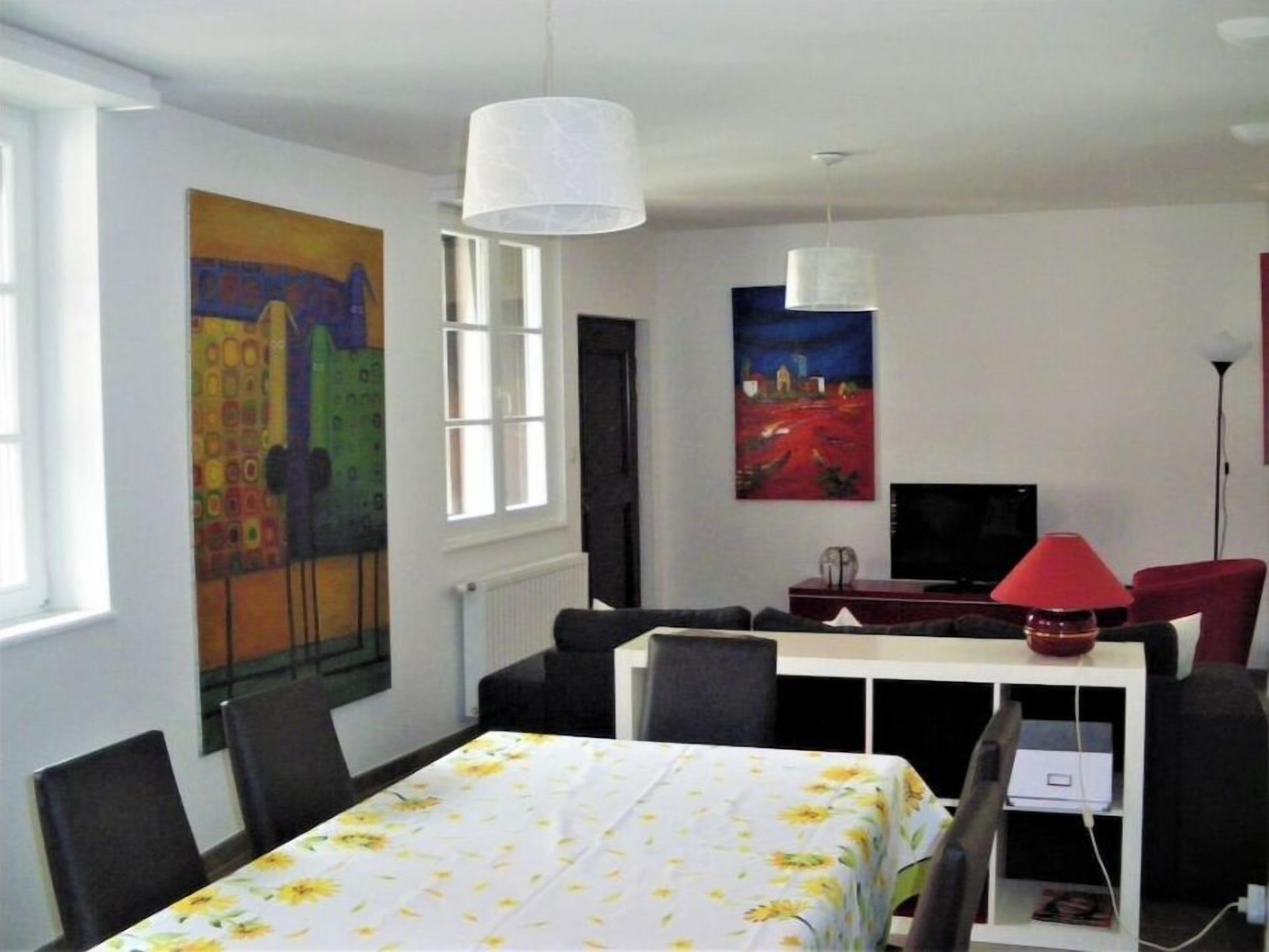 A room with a dining table, chairs, a TV, and artwork on the walls.