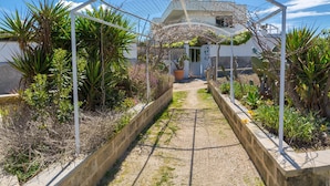 Un sentier de jardin agrémenté d’une arche en métal, entouré de différentes plantes et d’un pot de fleurs.