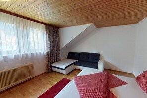 A bedroom with a loft bed, a sofa bed, a radiator, and a window with curtains.