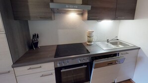 Een compacte keuken met een fornuis, oven en vaatwasser, houten kastjes en een koffiezetapparaat.
