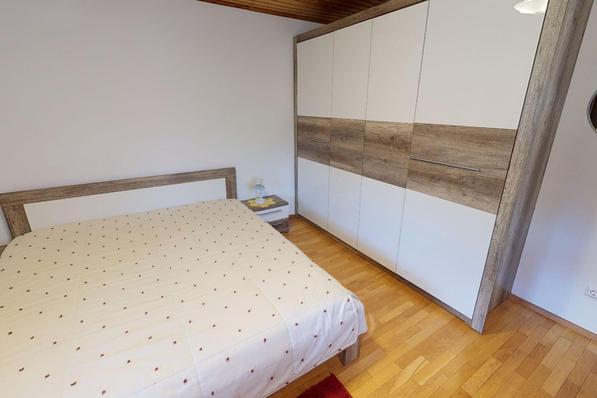 Un dormitorio con cama, cabecero de madera, armario con diseño de paneles de madera y una mesita de noche con lámpara.