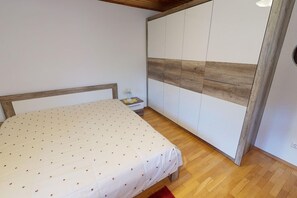 A bedroom with a bed, wooden headboard, a wardrobe with a wooden panel design, and a small bedside table with a lamp. - Holiday Home Bodensdorf near Ski & Lake (Bodensdorf am Ossiachersee)