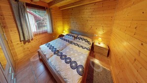 Ein Schlafzimmer einer Holzhütte mit einem Bett, zwei Nachttischlampen und einem Fenster mit Vorhängen.