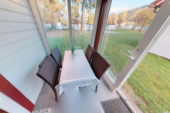 A covered patio with a table and chairs, a view of a grassy yard, and a door to the right.