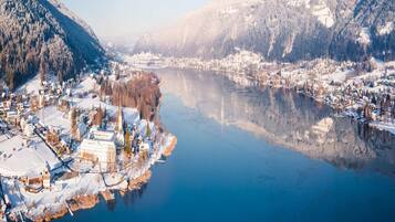 Winterliche Landschaft mit Fluss, schneebedeckten Gebäuden und Bergen.