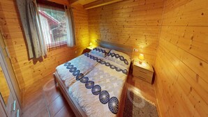 A wooden cabin bedroom with a bed, nightstands, and a window with curtains. - Holiday Home Bodensdorf near Gerlitzen Ski Area (Bodensdorf am Ossiachersee)