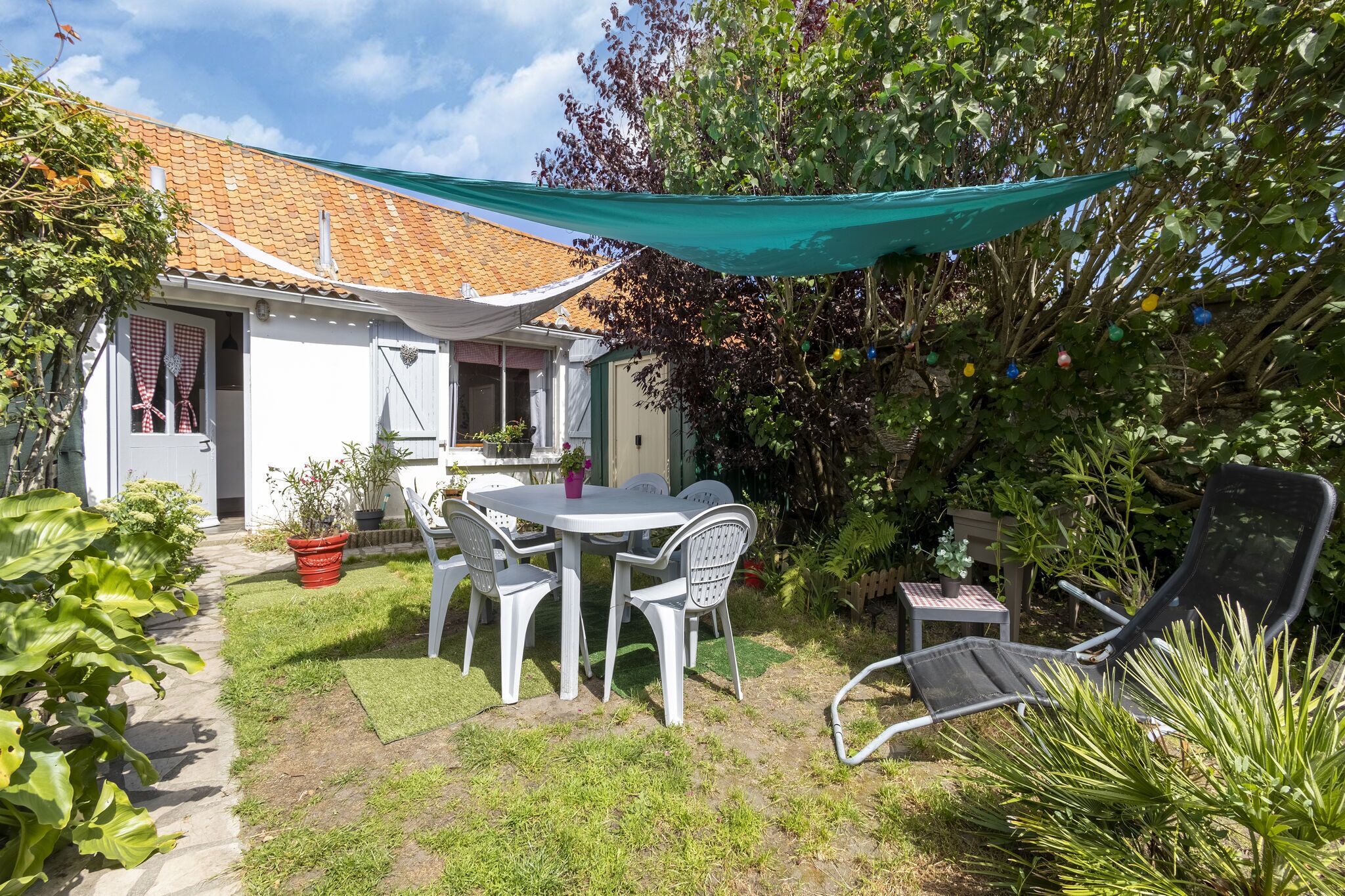A patio with a table and chairs, a garden, and a house with a tiled roof.