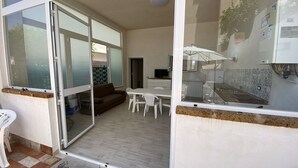 Eine offene Schiebetür führt zu einem Essbereich mit Tisch und Stühlen, einer Couch und einer sichtbaren Küchenzeile mit Spüle und Arbeitsplatte.