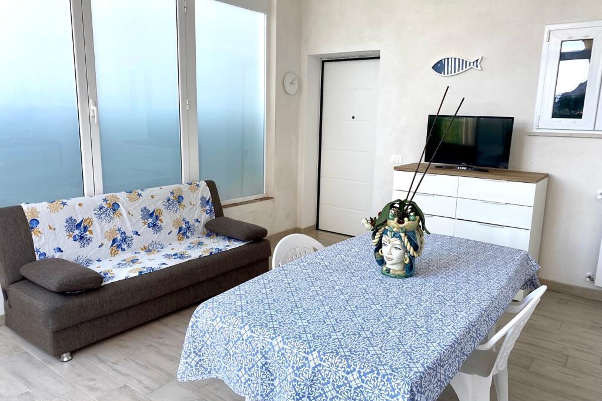 A living room with a sofa, a dining table, a television on a cabinet, and a decorative fish on the wall.