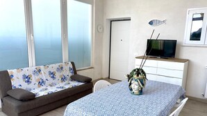 Ein Wohnzimmer mit einer Couch, einem Esstisch, einem Fernseher auf einem Schrank und einem dekorativen Fisch an der Wand.