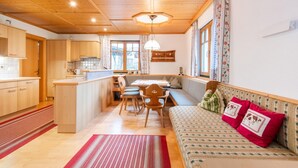A cozy kitchen with wooden cabinets, a dining area with a table and chairs, and a sofa with decorative pillows. - Holiday apartment in Kaltenbach (Kaltenbach)
