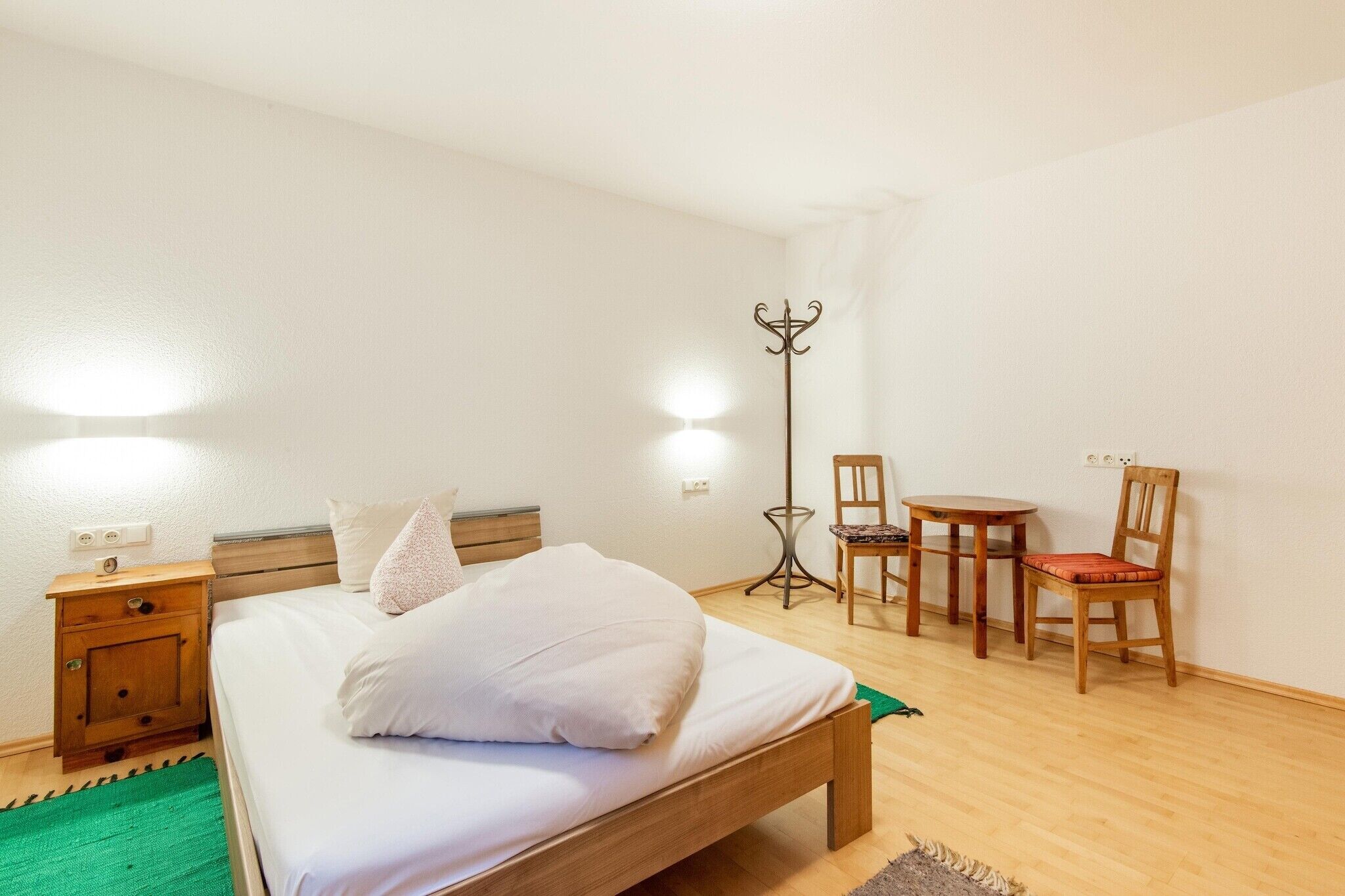 A bedroom with a wooden bed, a nightstand, a chair, a small table, and a floor lamp.