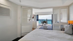 A hotel room with a large bed, a balcony with a view of the sea, and white shutters. - Oceanfront Resort: Heated Pool & Spa (Golden Beach)