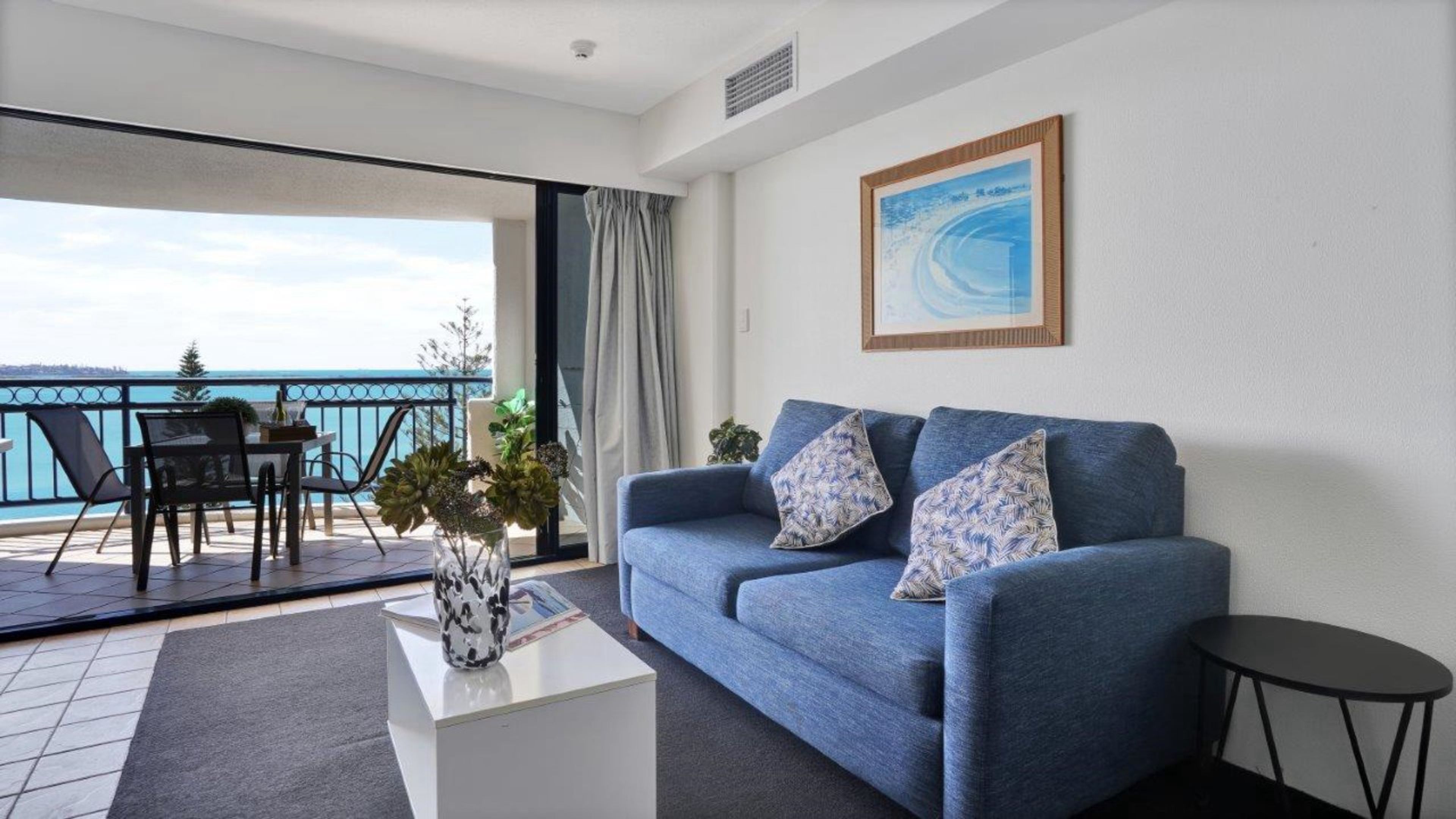 Een woonkamer met een bank, een salontafel en uitzicht op de zee vanaf een balkon.