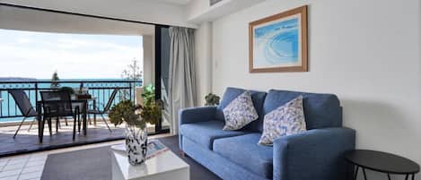 Een woonkamer met een bank, een salontafel en uitzicht op de zee vanaf een balkon.