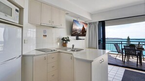 A modern kitchen with a built-in microwave, a sink, and a small countertop. There is a potted plant on the counter and a flat-screen TV mounted on the wall.
