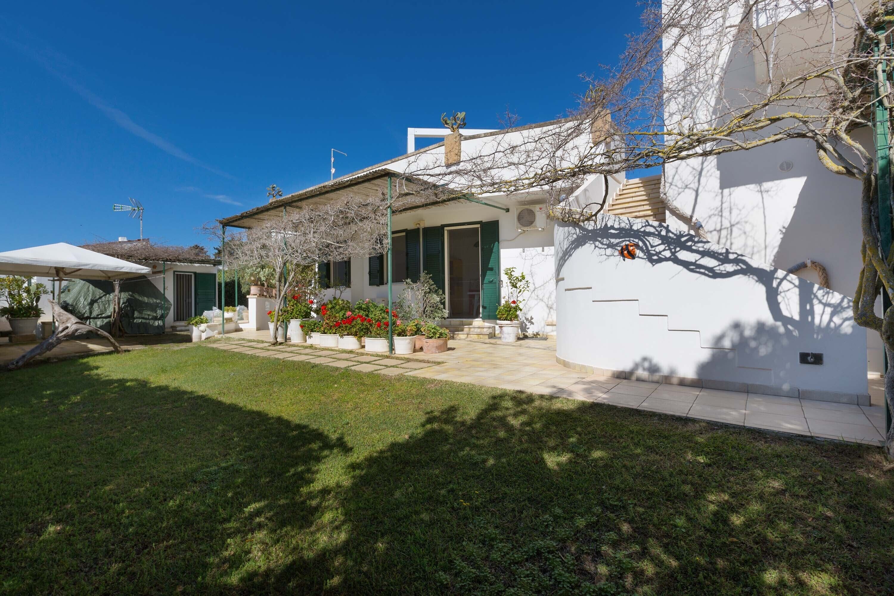 A white house with a covered patio, a small garden, and a staircase leading to the entrance.