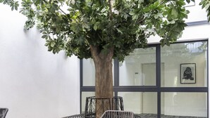An outdoor seating area with wicker furniture and a large tree. - Village by Maier - kontaktloser Check-in (Hohenems)