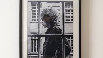 Une photographie en noir et blanc, encadrée, représentant une personne debout devant une fenêtre.