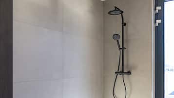 Eine moderne Dusche mit Duschbrause und Reinigungsbürste, ein großes Fenster mit Aussicht und eine Tür mit Griff.