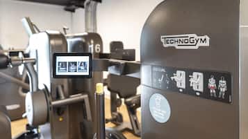 Un gimnasio con diversas máquinas de ejercicio, incluyendo una máquina para curl de piernas con la etiqueta 'TECHNOGYM'.