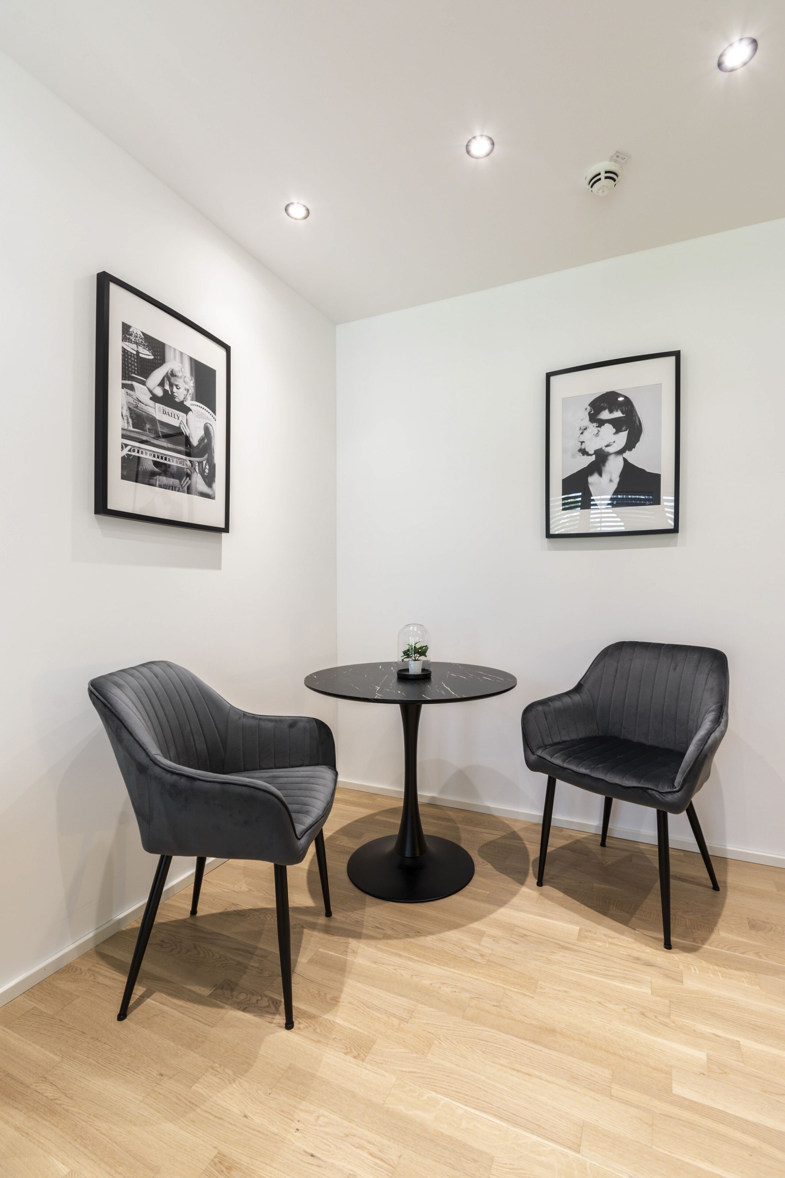 A room with two black chairs, a small round table, and two framed black-and-white photographs on the walls.