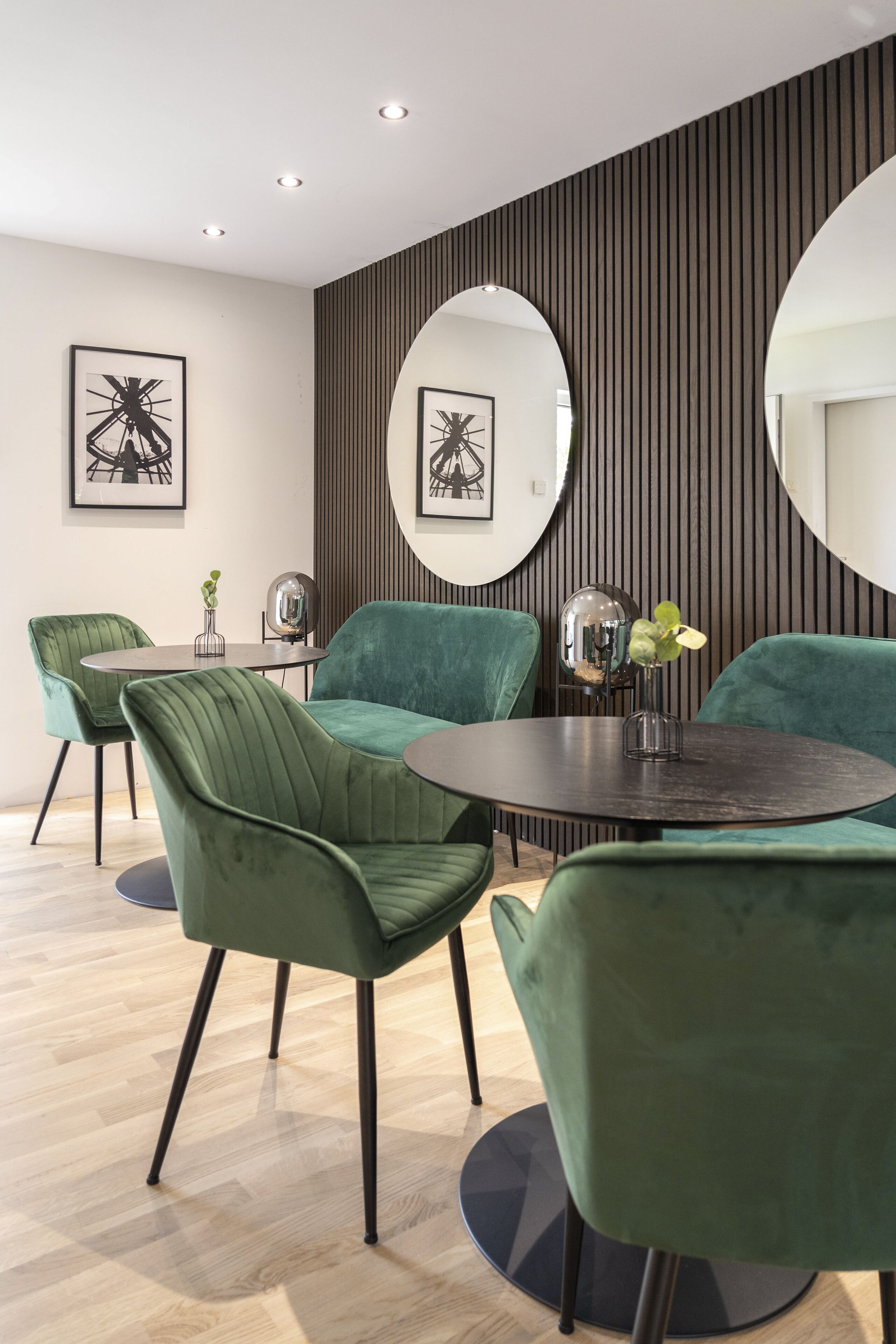 A modern dining area with green upholstered chairs, a round table, and two large mirrors on the wall.
