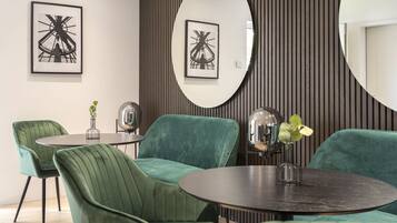 A modern dining area with green upholstered chairs, a round table, and two large mirrors on the wall.