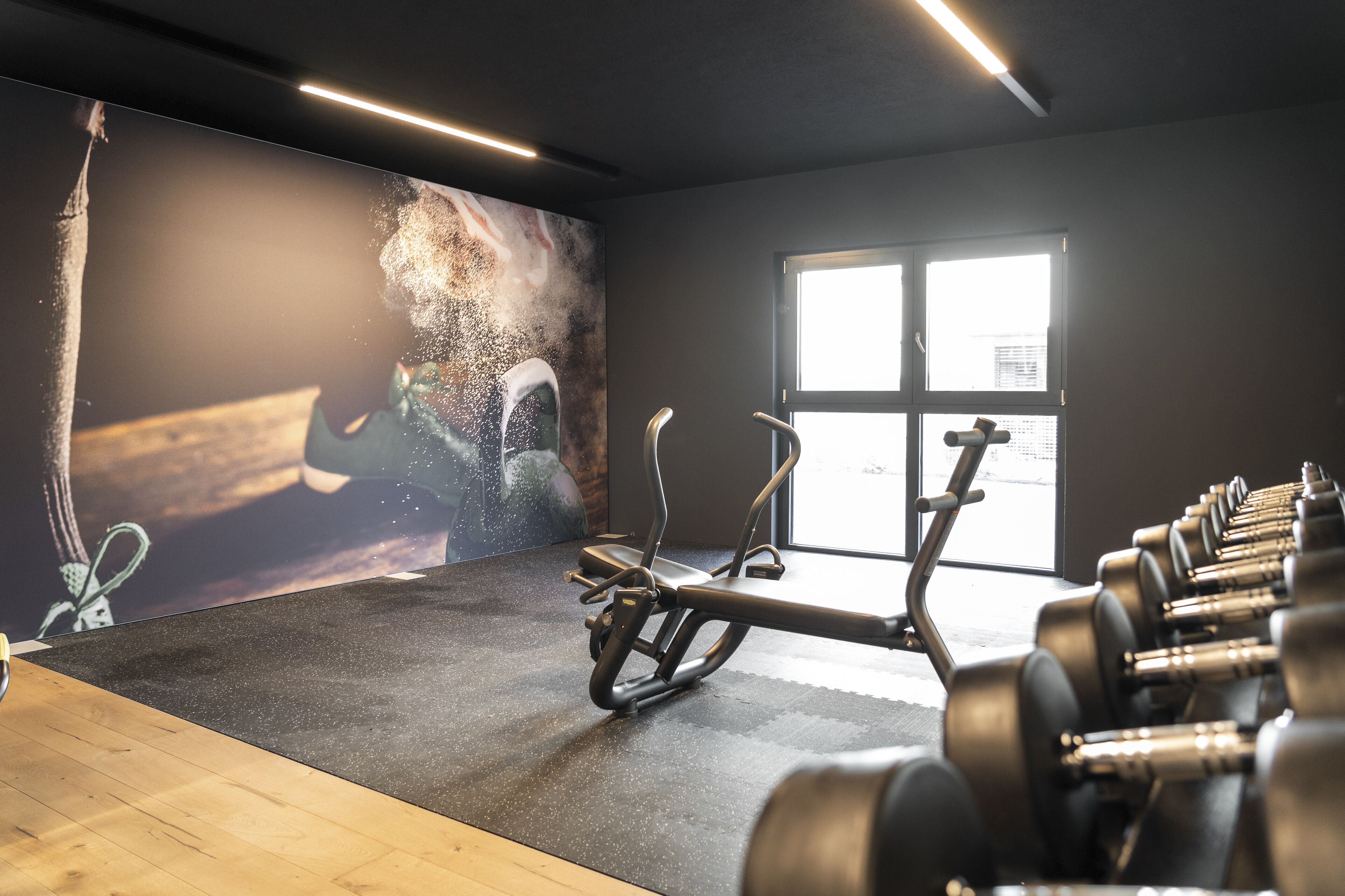 Un gimnasio con equipo de ejercicio, un ventanal grande y un mural en la pared.