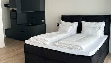 Ein modernes Schlafzimmer mit einem schwarzen Bett, weißer Bettwäsche und einem integrierten schwarzen Wandschrank mit Mikrowelle.