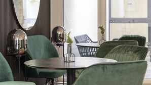 A modern dining area with green upholstered chairs, a round table, and a large mirror. - Village by Maier - kontaktloser Check-in (Hohenems)