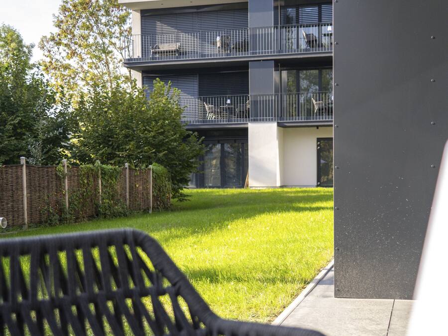 A modern building with a flat roof, a balcony, and a well-maintained lawn.
