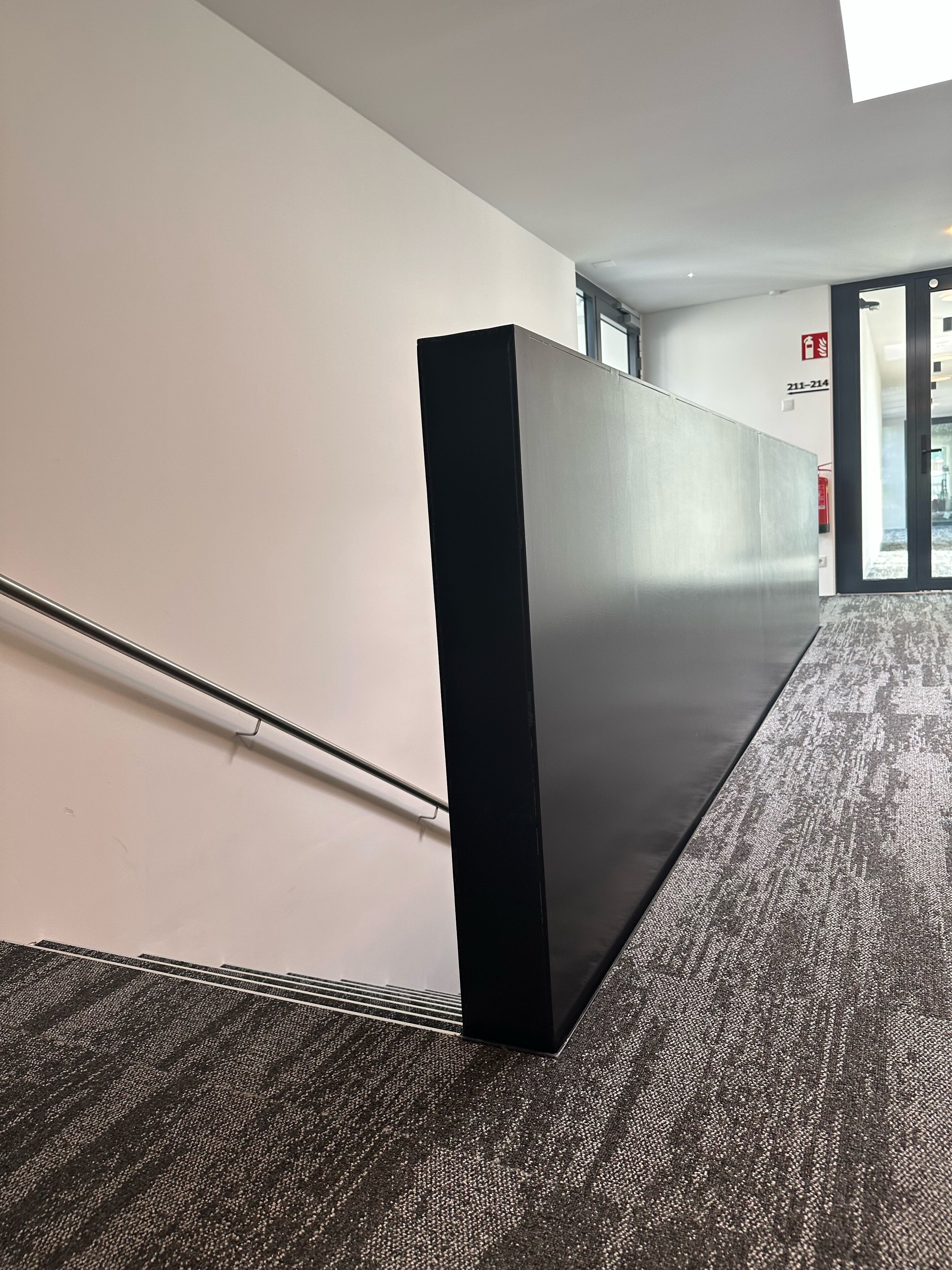 A modern interior with a black partition, a metal handrail, and a carpeted floor.