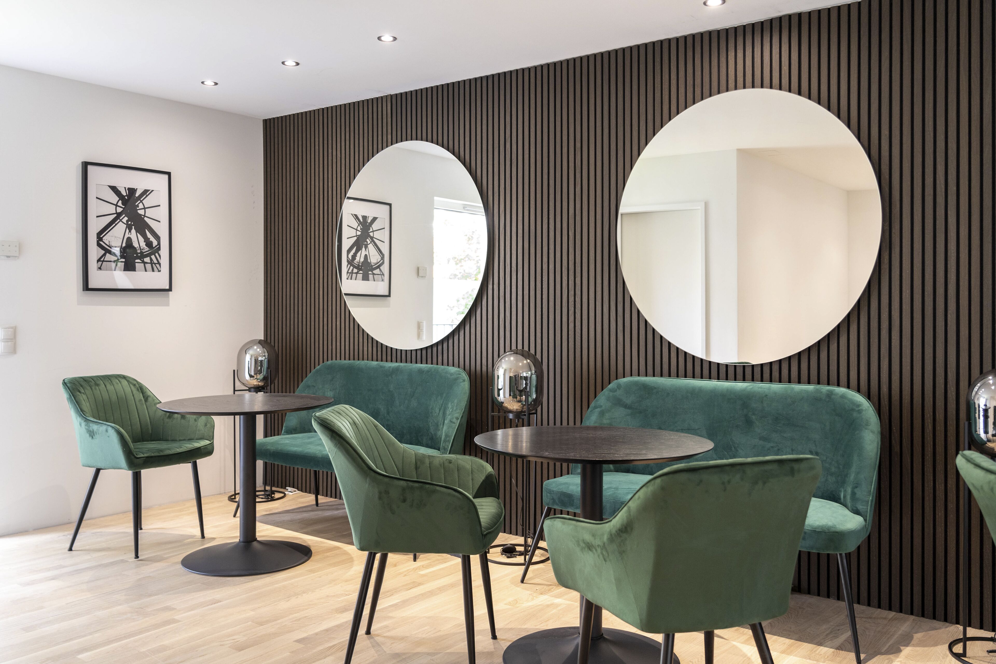 A modern interior with green upholstered chairs, a round table, and two large wall mirrors.