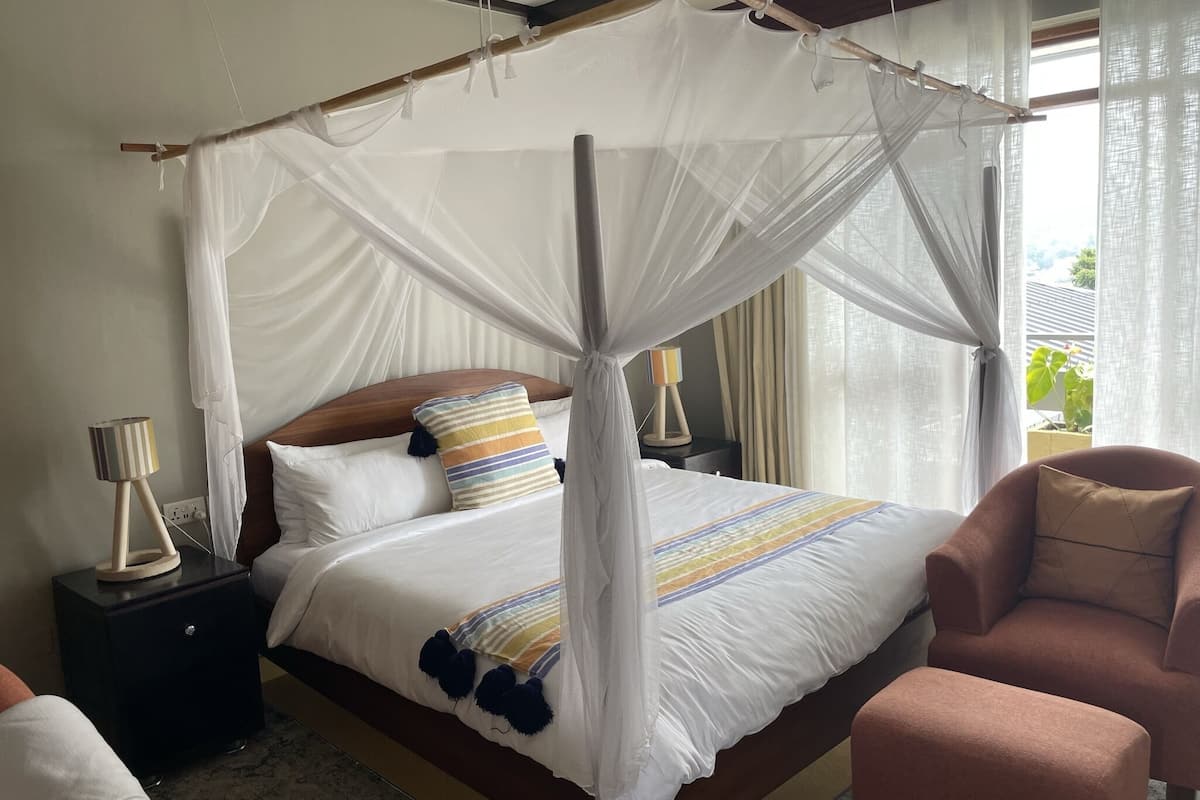 A bedroom with a four-poster canopy bed, a bedside lamp, a chair, and a nightstand.