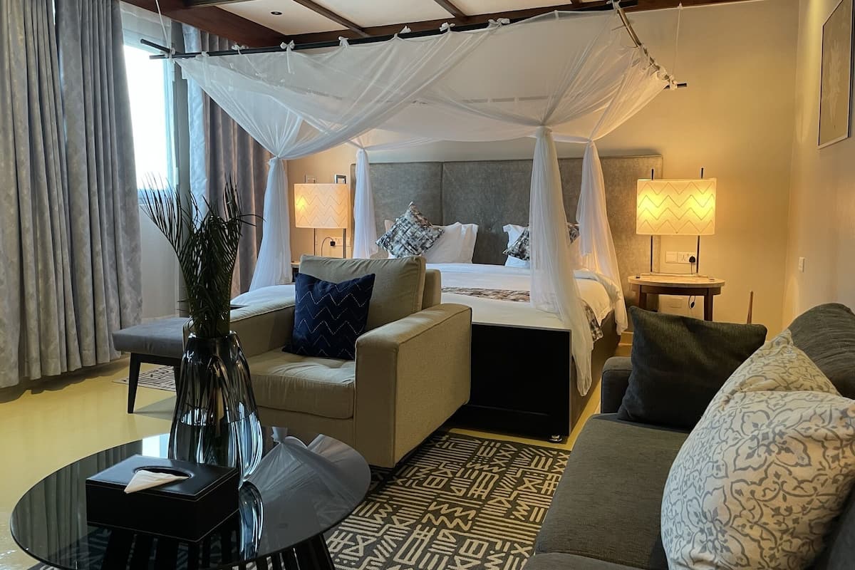 A hotel room with a bed under a canopy, a sofa, a coffee table, and a lamp.