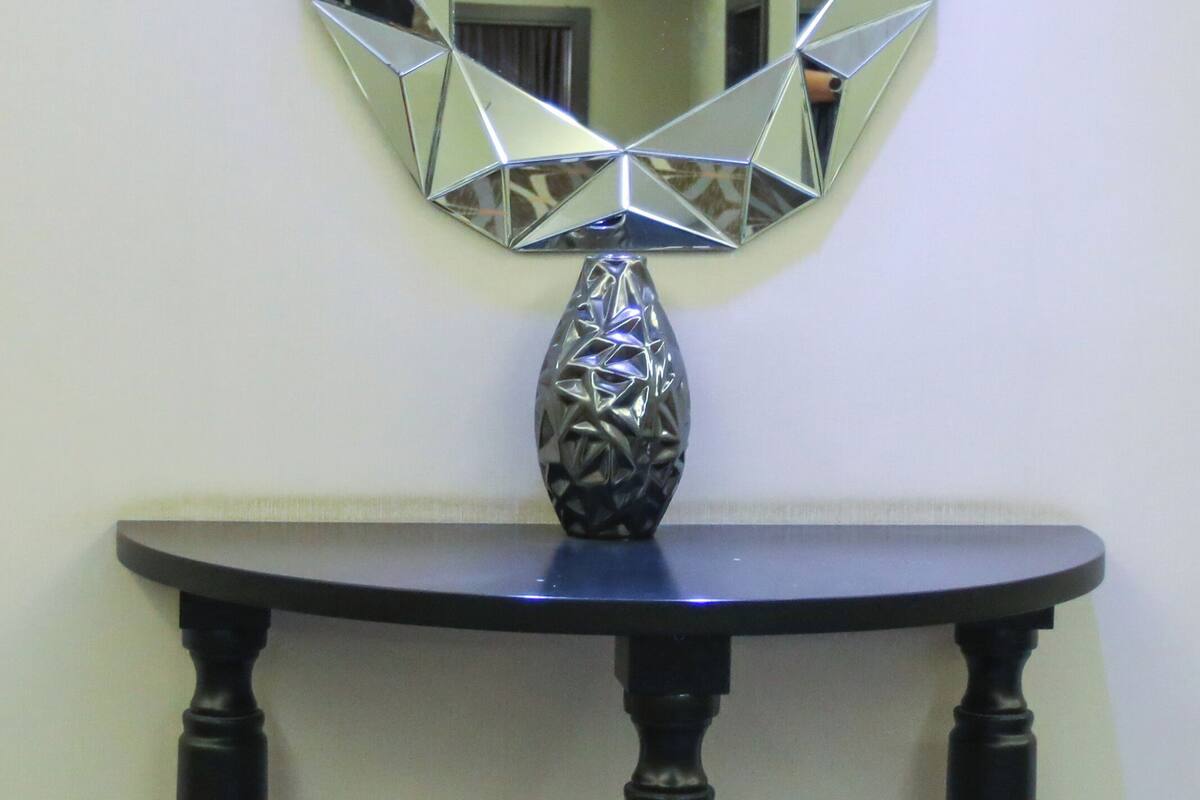 Una mesa redonda con un jarrón decorativo, un espejo hexagonal en la pared y un suelo estampado.