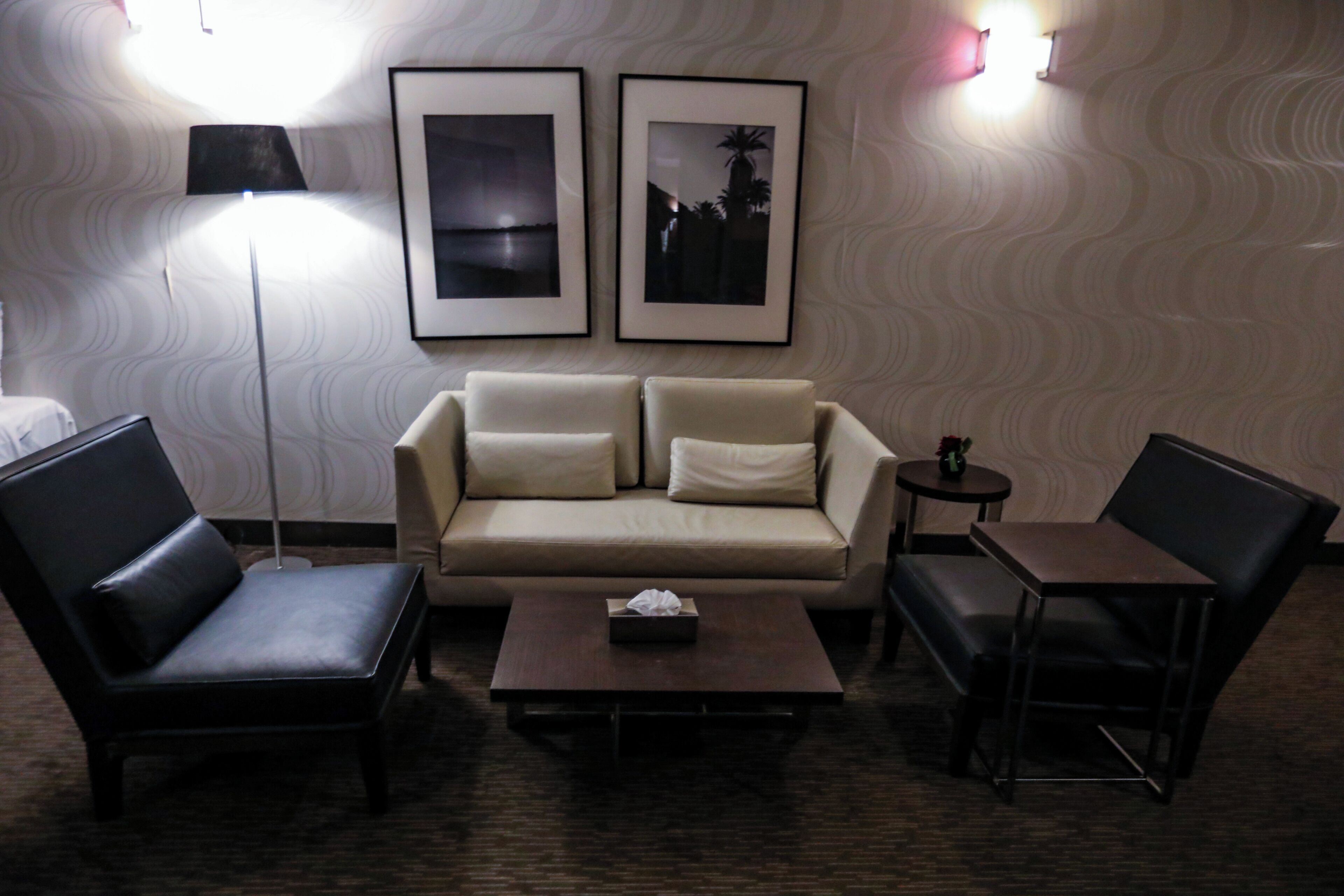 A hotel room with a sofa, two armchairs, a coffee table, a lamp, and two framed pictures on the wall.